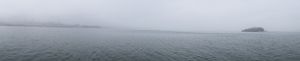 Misty gray seascape with calm waters extending to foggy horizon.