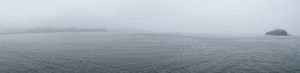 Panoramic view of foggy ocean horizon with overcast sky.