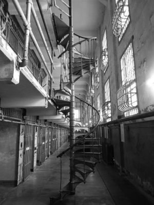 Black and white photographs showing empty prison cell block corridors with barred cells and metal railings.