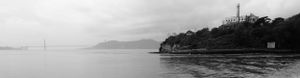 Black and white panoramic seascape showing a rocky coastline and calm waters.