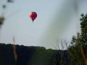 Red hot air balloon floating in a hazy sky above a tree-lined horizon.