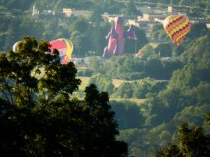 Colorful hot air balloons floating over a green valley landscape at sunrise.