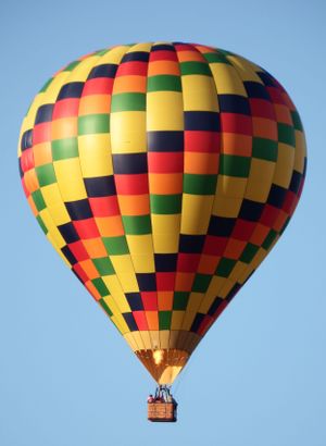 Colorful hot air balloon with checkered pattern in yellow, red, green and blue floating against clear blue sky.