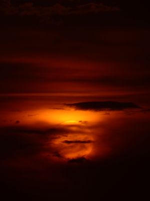 Fiery orange sunset glowing through dark storm clouds in the night sky.