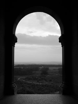 View through stone archway overlooking misty countryside landscape in black and white.