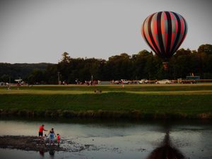 Hot air balloon landing near a lake with spectators watching from the shore.