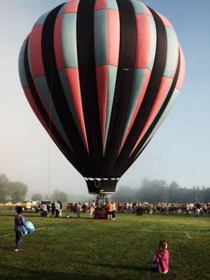 Large red and black striped hot air balloon being prepared for launch in a misty field.