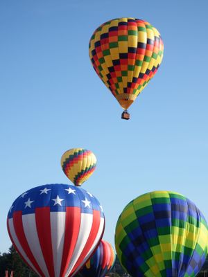 Collection of hot air balloons including patriotic American flag designs against blue sky.
