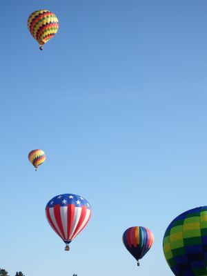 Colorful hot air balloons float against a bright blue sky during a balloon festival.