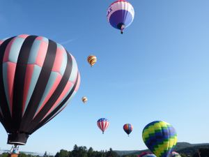 Multiple hot air balloons including a patriotic American flag design soar in the clear blue sky.