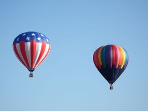 Red, white and blue hot air balloons drift through a cloudless summer sky.