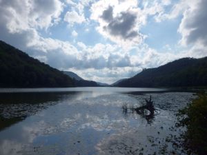 Dramatic clouds reflect on a serene lake surface surrounded by mountains.