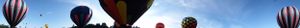 Panoramic view of hot air balloons ascending into a bright blue sky.