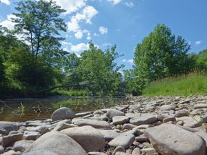 Rocky shoreline with large boulders under blue summer sky and white clouds.