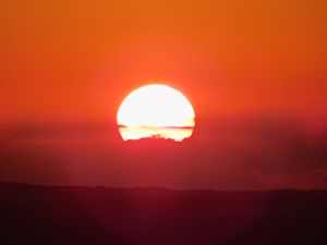 Time-lapse sequence of orange sunset with sun descending below dark horizon.