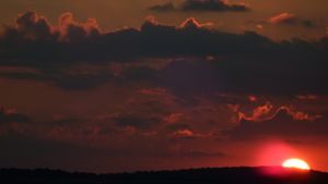 Dramatic orange and red sunset with dark clouds and glowing sun on horizon.