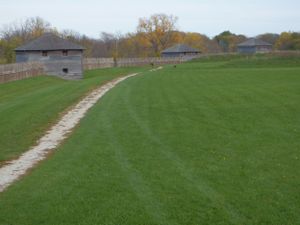 Historic blockhouse structure with a dirt path winding through manicured green lawn.