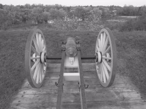 Historic cannon with large wooden wheels positioned on wooden platform in black and white.