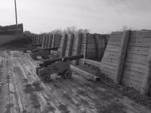 Historic cannons line up along wooden fortification walls at a military installation.