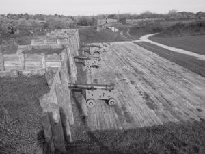 Bird's eye view of historic fort walls with mounted cannons and a curved road below.