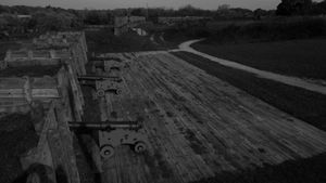Elevated view of fort battlements with cannons positioned along wooden defensive walls at dusk.