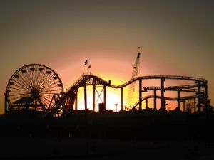 Silhouettes of amusement park rides and a Ferris wheel against a sunset sky.