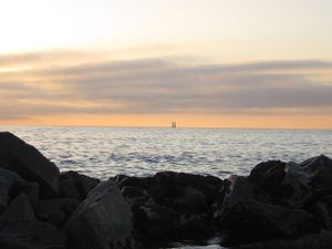 Rocky coastline at sunset with calm ocean waters stretching to the horizon.