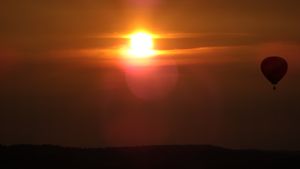 Dramatic orange sunset over silhouetted hills with hot air balloon in distance.