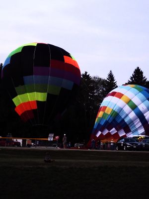 Colorful hot air balloons being inflated on a grassy field at dusk.
