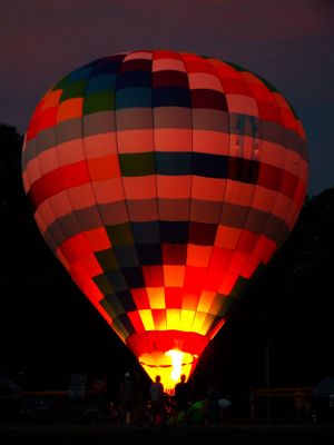 Hot air balloon glowing bright red and orange against dark twilight sky.