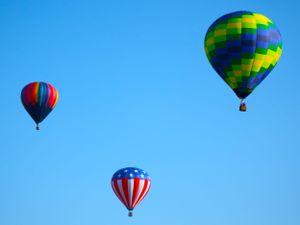 Hot air balloons floating in bright blue sky including one with American flag design.