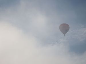 A single hot air balloon floats in an overcast grey sky with cloudy conditions.