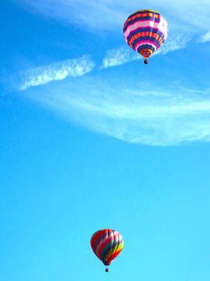 Red and white striped hot air balloons float serenely in a bright blue summer sky with wispy clouds.