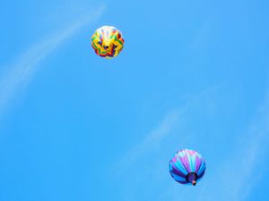 Colorful hot air balloons floating against a bright blue sky during a balloon festival.