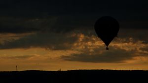 Hot air balloons silhouetted against a dramatic sunset sky with dark clouds.