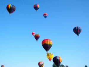 Hot air balloons with vibrant patterns floating in formation across a clear blue sky.