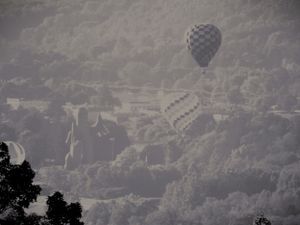 A black and white checkered hot air balloon floats among misty clouds in the sky.