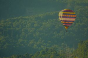A colorful striped hot air balloon soars over a forested hillside.