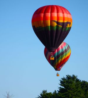 Two colorful hot air balloons with geometric patterns ascending in a clear blue sky.