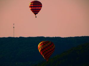 Two hot air balloons with red and black patterns float against a dusky pink sky.