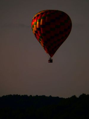 A red and black checkered hot air balloon silhouetted against a dark evening sky.