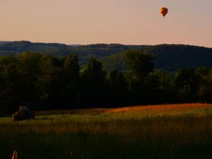 A single hot air balloon floats over a rural hillside at golden hour.