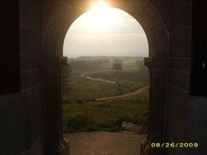 Sunlit landscape view through an arched stone window opening.