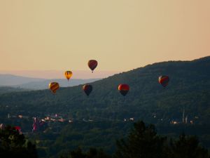 Colorful hot air balloons floating over mountain landscape at dusk.