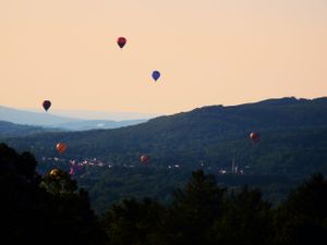 Multiple hot air balloons dot the twilight sky over a mountain valley.