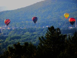 Hot air balloons float against blue mountains and sky during a festival.