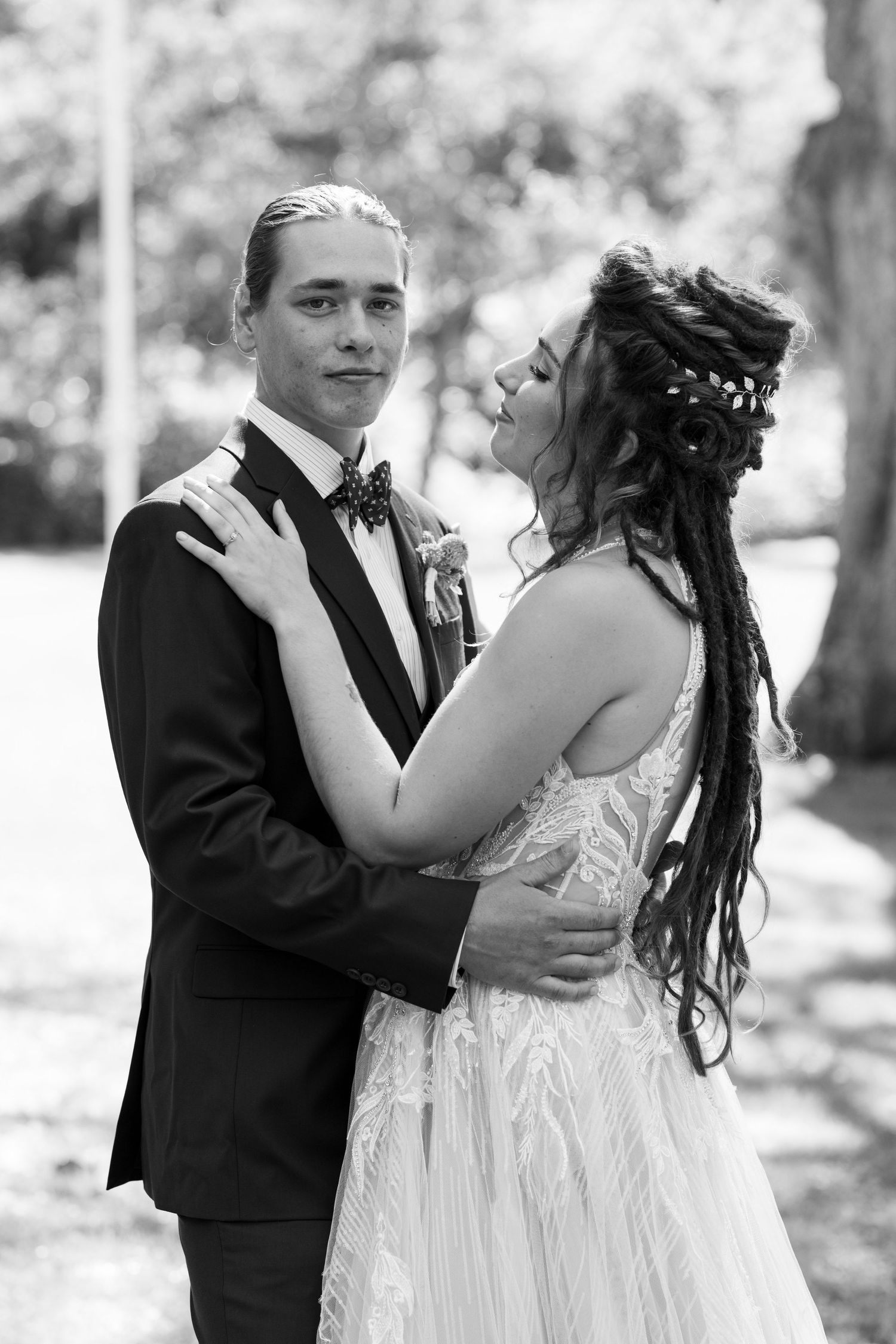 A romantic black and white wedding photo showing a couple embracing outdoors, with the bride in white and groom in tuxedo.