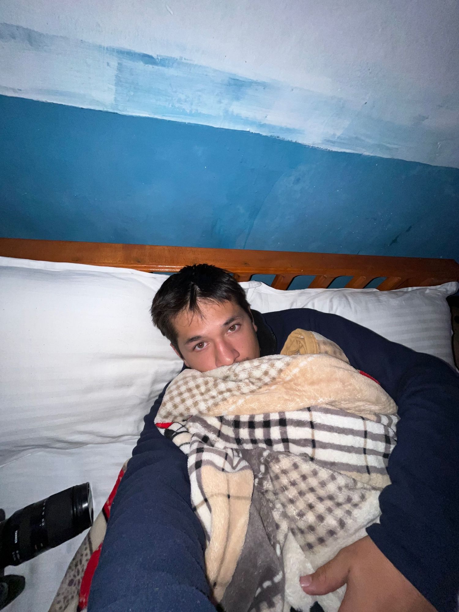 Person sleeping under checkered blankets in a basic mountain shelter.