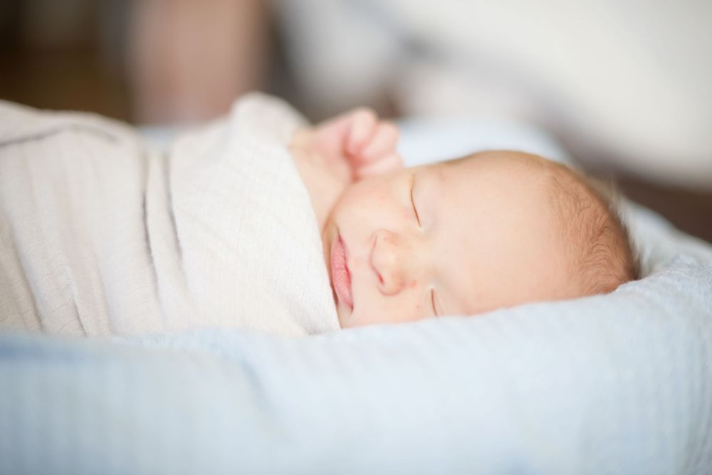 Sleeping infant swaddled in white blanket resting on light blue bedding.