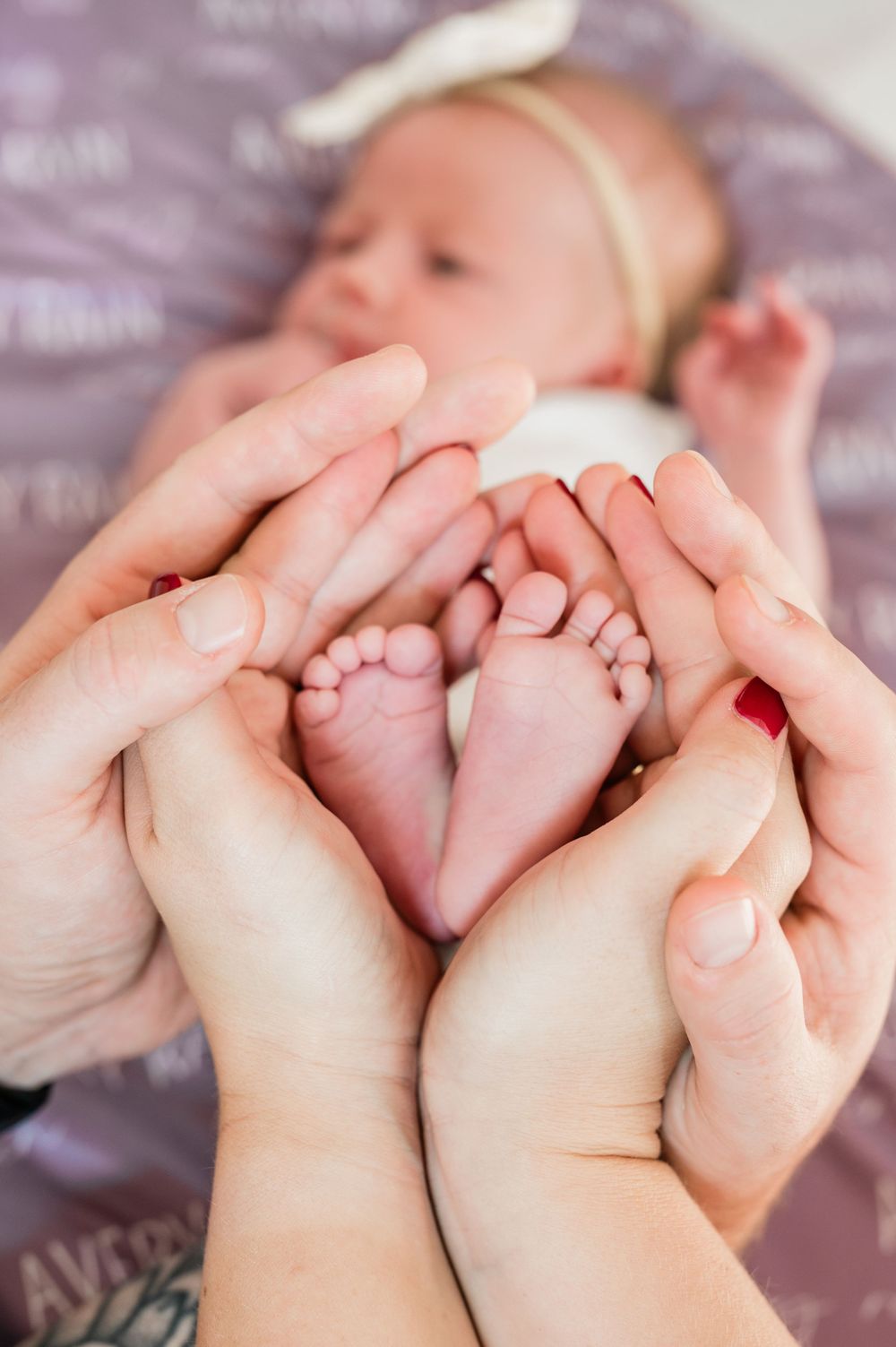 Parents cradling their newborn baby's tiny feet in their hands, forming a heart shape, with infant resting on blanket.